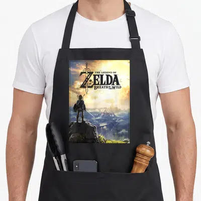 Horizon legend apron - Link standing on rock facing castle with title text over sword in blue gold grey yellow — shown on a black cotton canvas apron against a white background