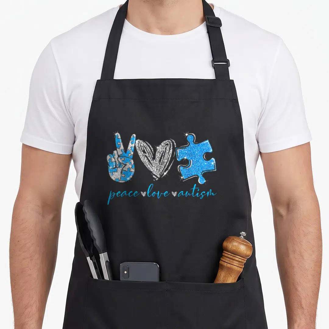 Peace puzzles lover apron - Blue and white peace sign, heart, and puzzle piece with text below — shown on a black cotton canvas apron against a white background