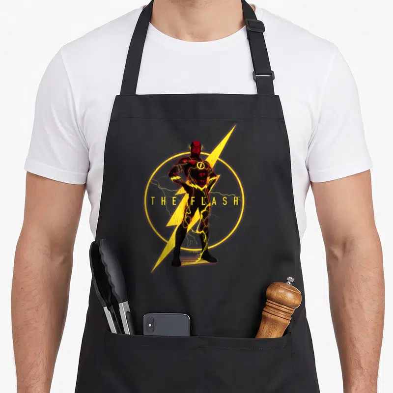 Justice lightning bolt apron - The Flash character standing over yellow lightning bolt and circle with printed text — shown on a black cotton canvas apron against a white background