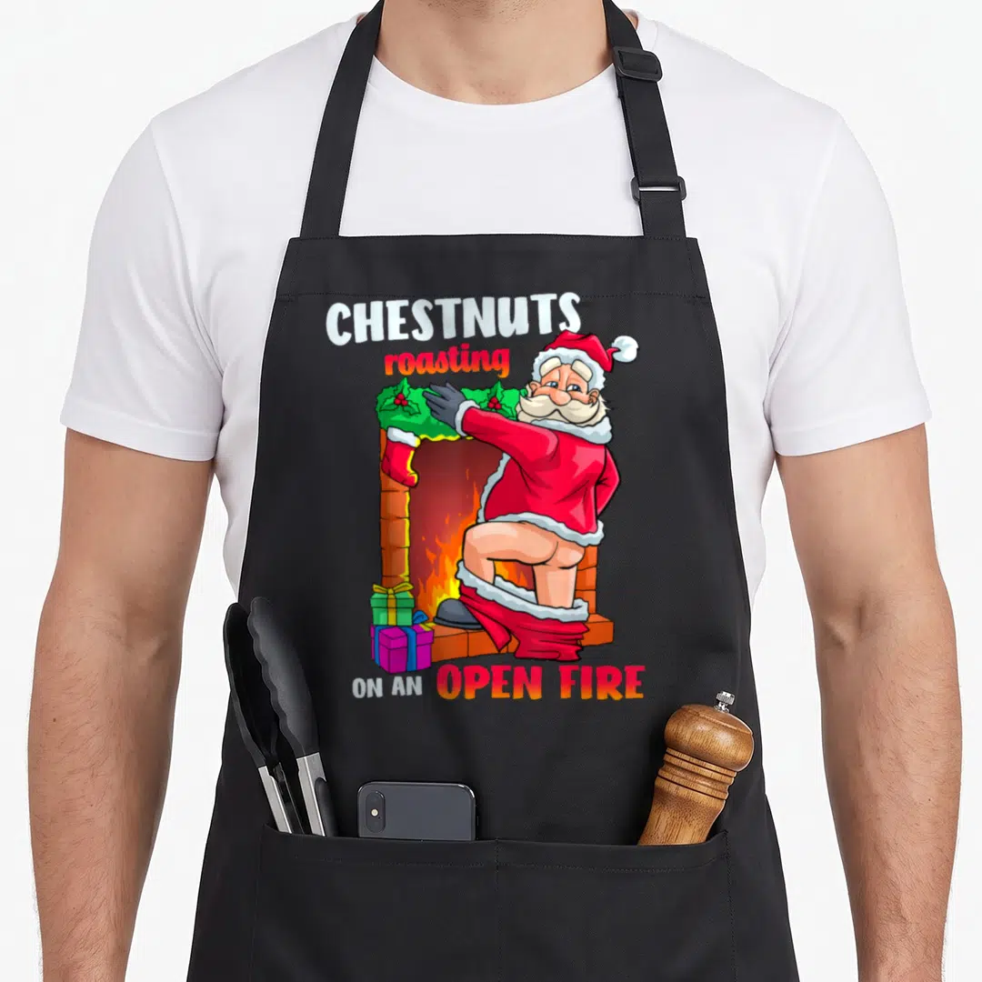 Chest the dirty apron - Cartoon Santa facing away from viewer with trousers down and fireplace text — shown on a black cotton canvas apron against a white background
