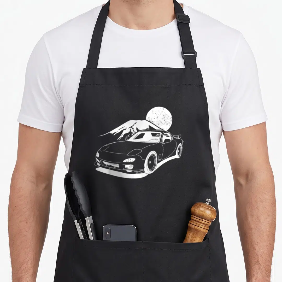Motorsport japan apron - White line-art tuning car silhouette in front of a mountain and textured sun circle — shown on a black cotton canvas apron against a white background