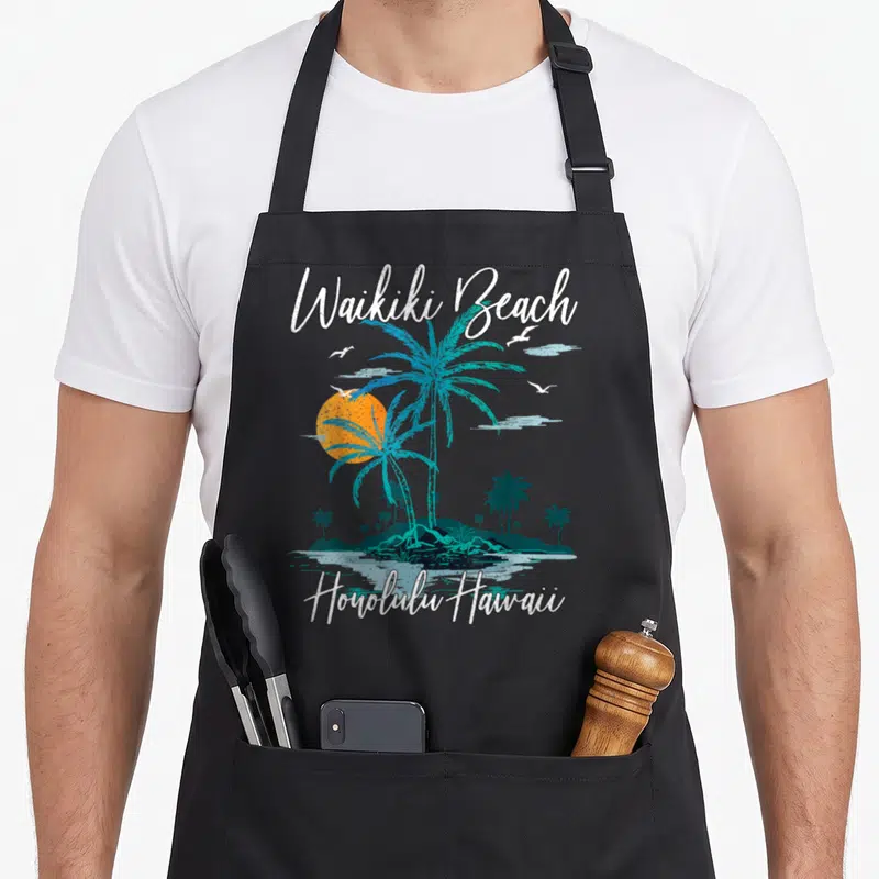 Sunset family aprons - Retro Waikiki Beach text over teal palm trees and orange sun with Honolulu Hawaii label — shown on a black cotton canvas apron against a white background