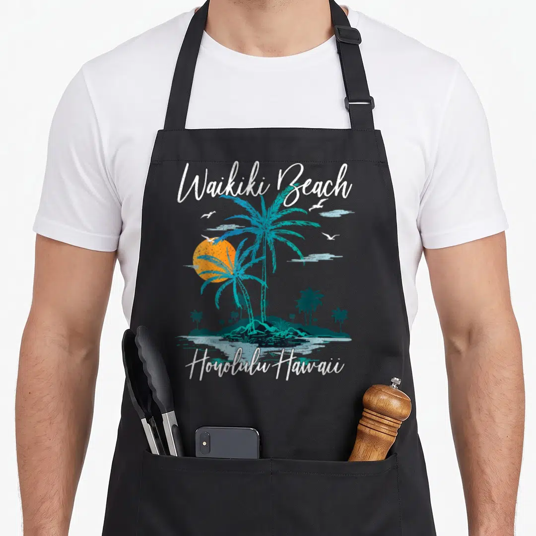 Sunset family aprons - Retro Waikiki Beach text over teal palm trees and orange sun with Honolulu Hawaii label — shown on a black cotton canvas apron against a white background