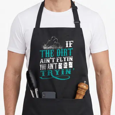 Barrel lace apron - Horse rider silhouette jumping hurdle with IF THE DIRT AIN'T FLYIN YOU AIN'T TRYIN' text in white — shown on a black cotton canvas apron against a white background