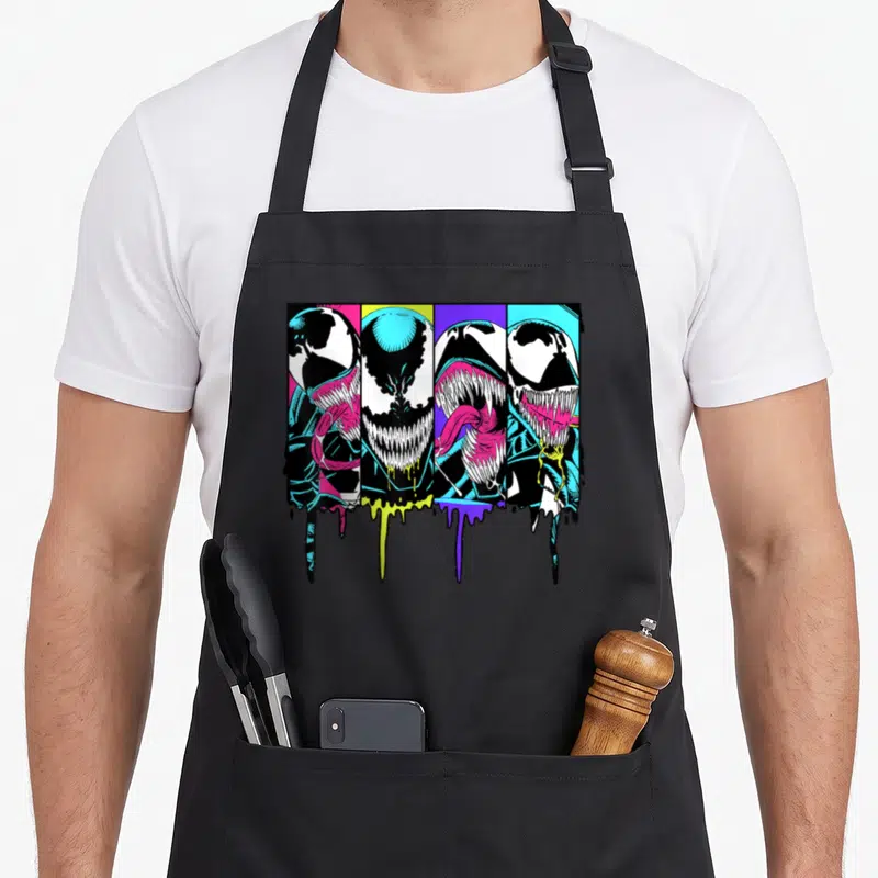 Dripping colorful apron - Four Venom heads in vertical panels with dripping paint in black, white, pink, yellow — shown on a black cotton canvas apron against a white background