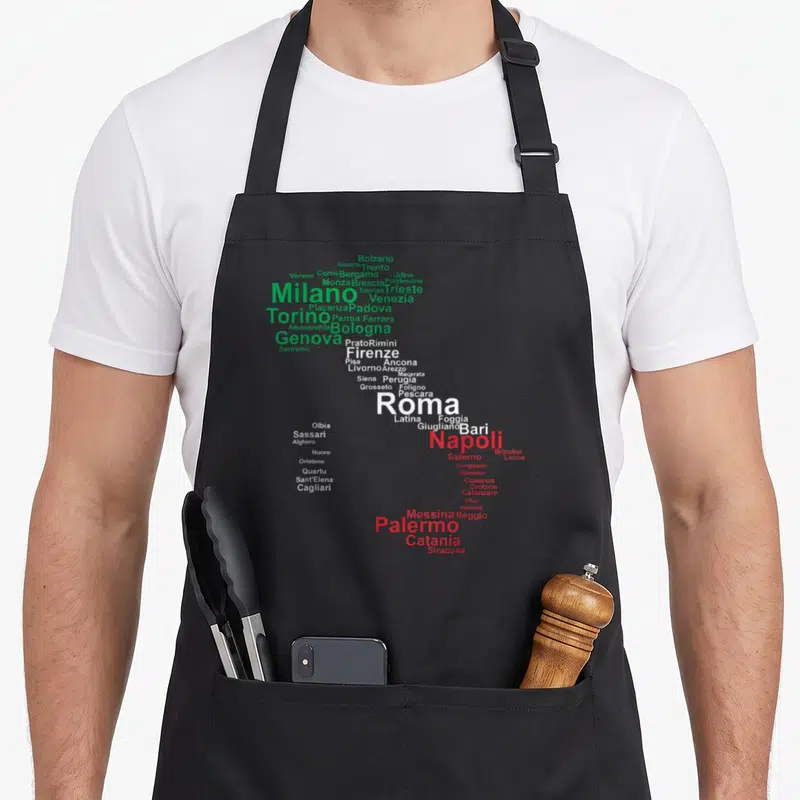 Travel italy apron - Italian city names forming a map shape in green white and red text — shown on a black cotton canvas apron against a white background