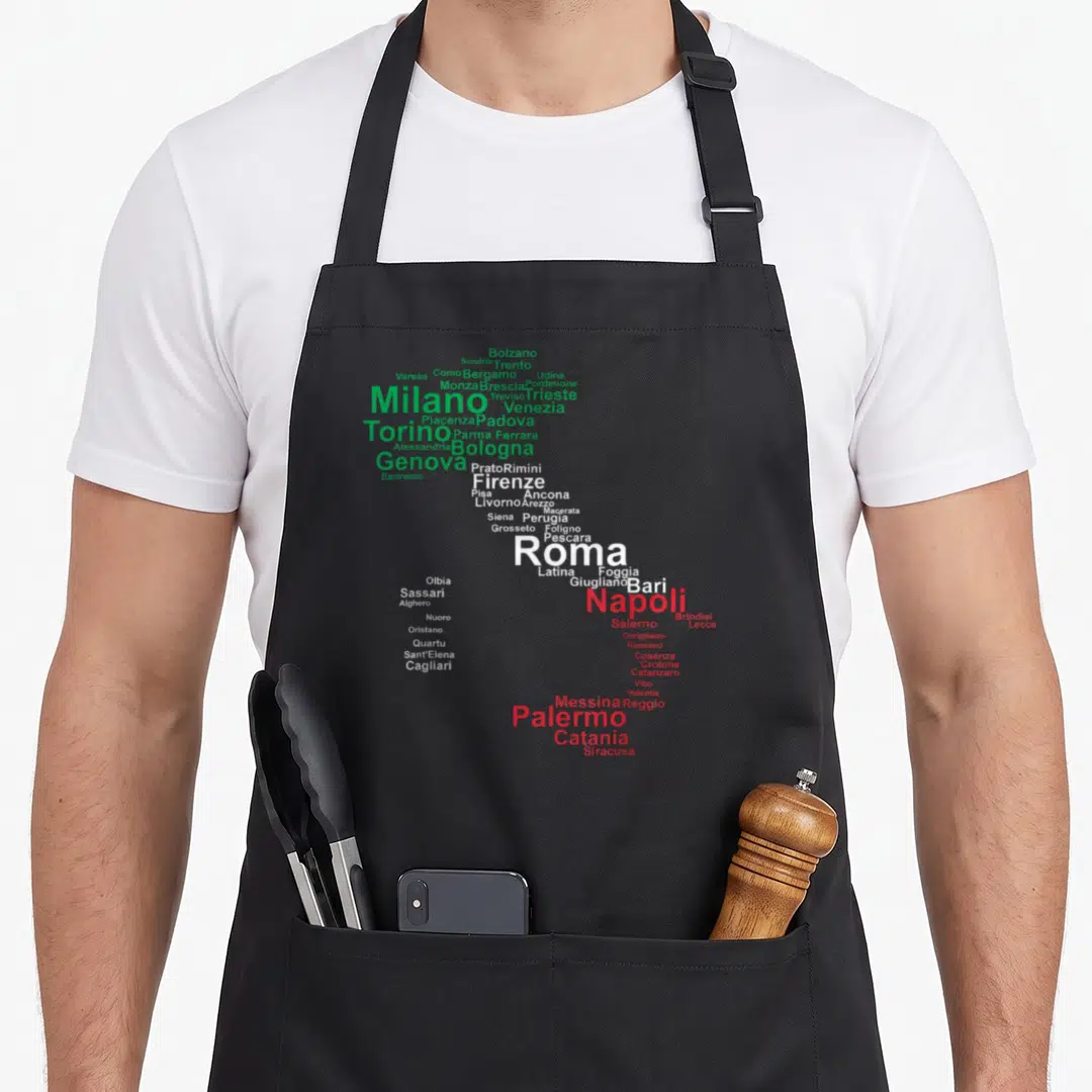 Travel italy apron - Italian city names forming a map shape in green white and red text — shown on a black cotton canvas apron against a white background