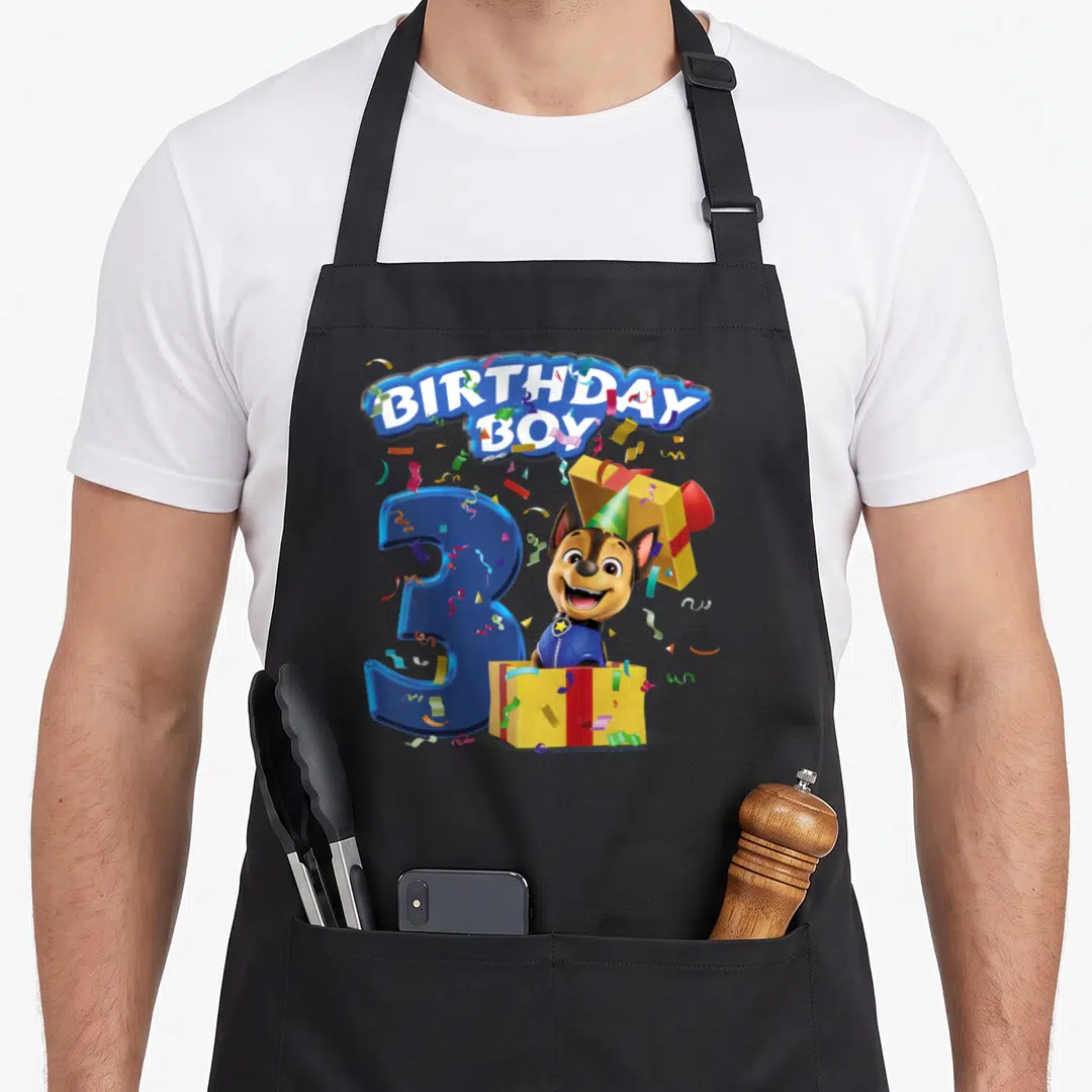 Cool chase birthday apron - BIRTHDAY BOY text, blue number 3, dog in yellow gift box with confetti — shown on a black cotton canvas apron against a white background