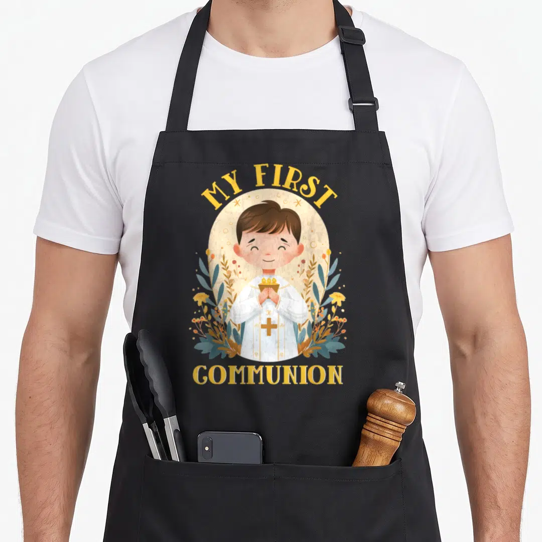 Funny 1st communion aprons - Cartoon boy holding chalice with MY FIRST COMMUNION text and blue-green floral designs — shown on a black cotton canvas apron against a white background