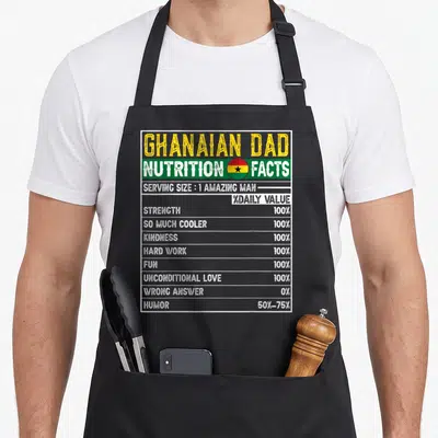 Ghanaian father day apron - Nutrition facts label with Ghana flag colors listing dad traits like strength and humor — shown on a black cotton canvas apron against a white background