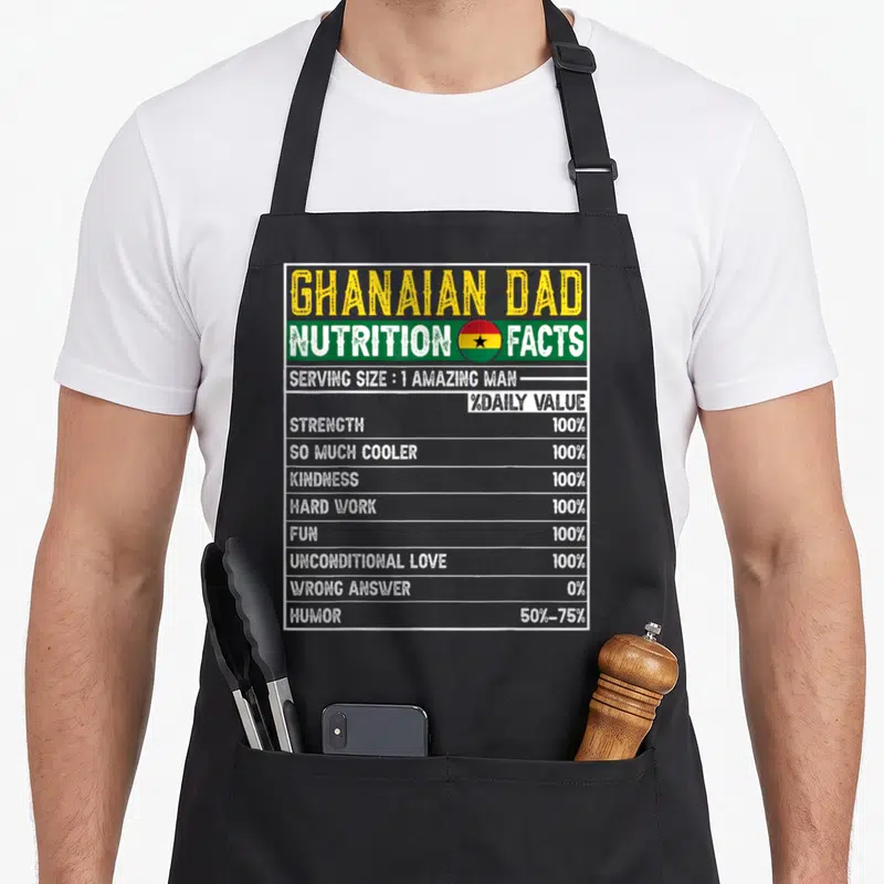 Ghanaian father day apron - Nutrition facts label with Ghana flag colors listing dad traits like strength and humor — shown on a black cotton canvas apron against a white background
