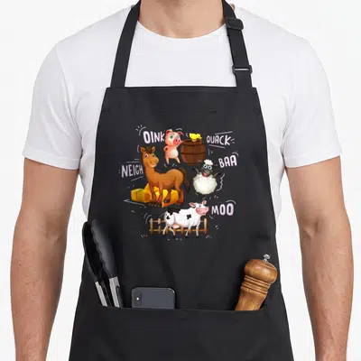 Sound farm aprons - Cartoon pig, duck, sheep, horse, cow with sound words OINK QUACK BAA NEIGH MOO and barn props — shown on a black cotton canvas apron against a white background