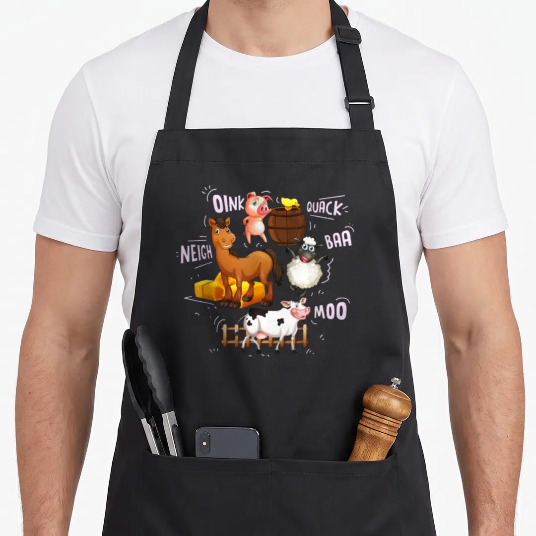 Sound farm aprons - Cartoon pig, duck, sheep, horse, cow with sound words OINK QUACK BAA NEIGH MOO and barn props — shown on a black cotton canvas apron against a white background