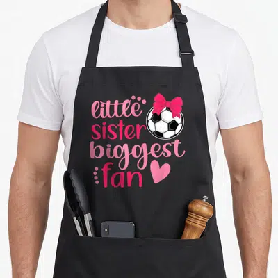 Sister soccer apron - Text reading little sister biggest fan next to a soccer ball with a pink bow — shown on a black cotton canvas apron against a white background