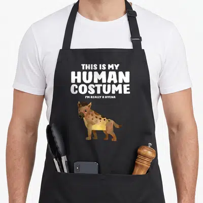 Human hyena apron - Cartoon hyena standing below stacked white text reading This Is My Human Costume I'm Really A Hyena — shown on a black cotton canvas apron against a white background