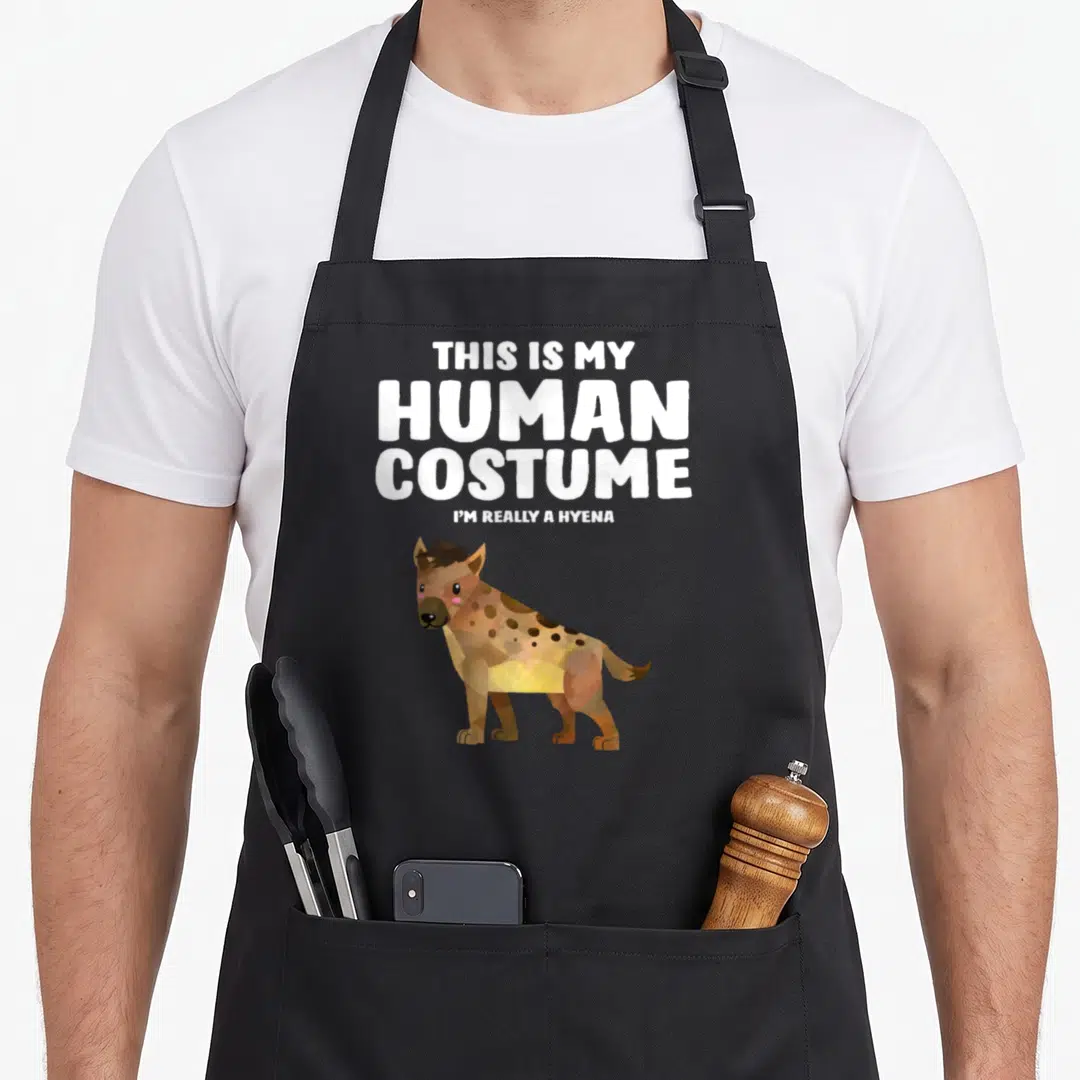 Human hyena apron - Cartoon hyena standing below stacked white text reading This Is My Human Costume I'm Really A Hyena — shown on a black cotton canvas apron against a white background