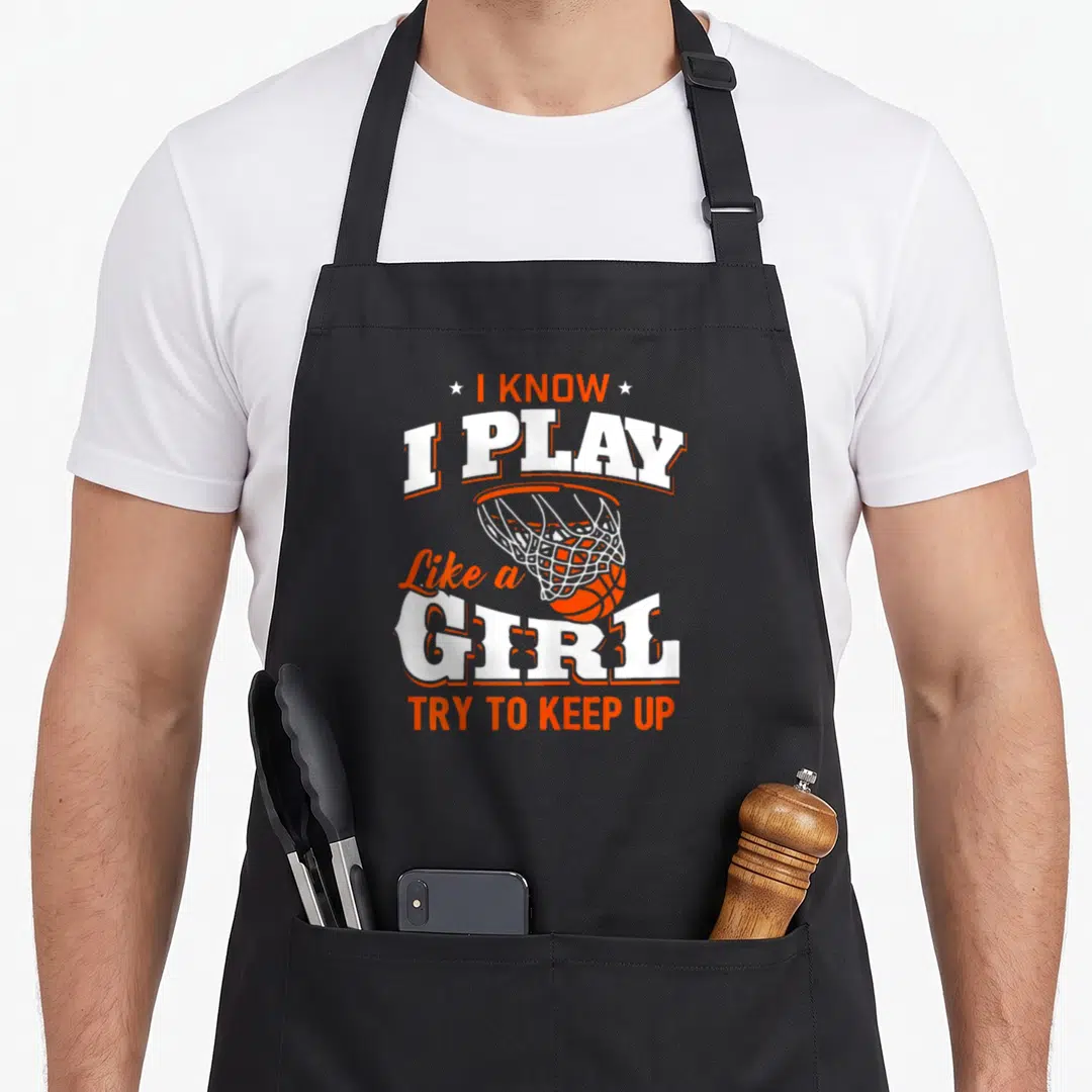 Play im jay apron - I Know I Play Like a Girl text surrounding an orange basketball hoop and net — shown on a black cotton canvas apron against a white background