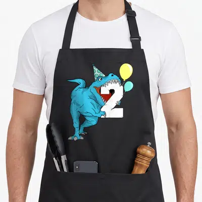 Dinosaur 2nd t-rex apron - Blue T-Rex biting white number 2, wearing polka dot party hat, two balloons yellow and light — shown on a black cotton canvas apron against a white background