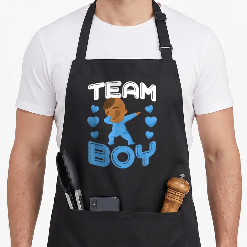 Gender uab kidkis apron - Cartoon baby dabbing with Team Boy text and blue hearts — shown on a black cotton canvas apron against a white background