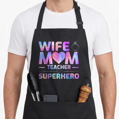 Superhero best teacher apron - Stacked WIFE MOM TEACHER SUPERHERO text with ring, heart, and lines in purple blue pink — shown on a black cotton canvas apron against a white background