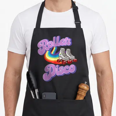 Roller disco 70s apron - Purple Roller Disco text with white skates and rainbow trail — shown on a black cotton canvas apron against a white background
