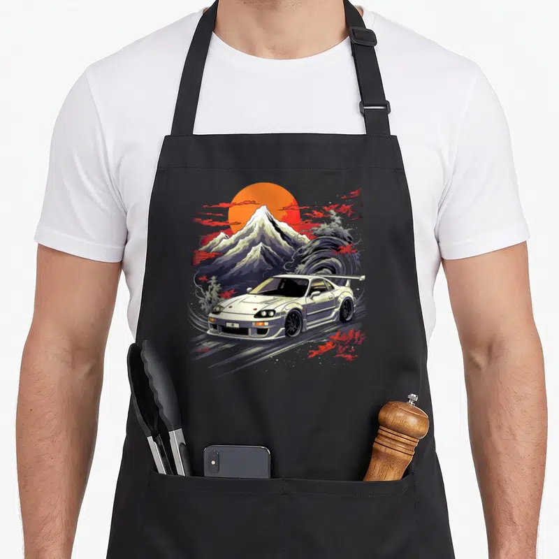 Legend car apron - White JDM coupe with orange sun, grey wave, red clouds, and snow-capped mountain in retro style — shown on a black cotton canvas apron against a white background