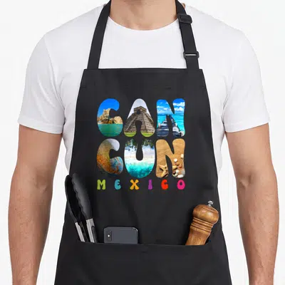 Cancun vacation mexico apron - CANCUN text filled with ruins and beach photos above colorful MEXICO letters — shown on a black cotton canvas apron against a white background
