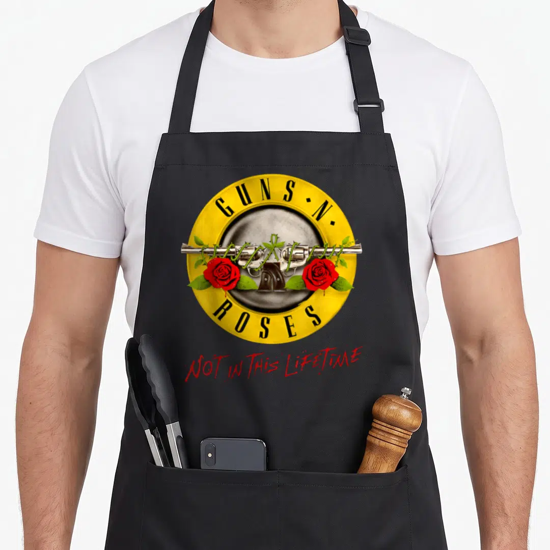 Lifetime gun apron - Crossed revolvers entwined with red roses inside yellow circle with GUNS N ROSES text — shown on a black cotton canvas apron against a white background
