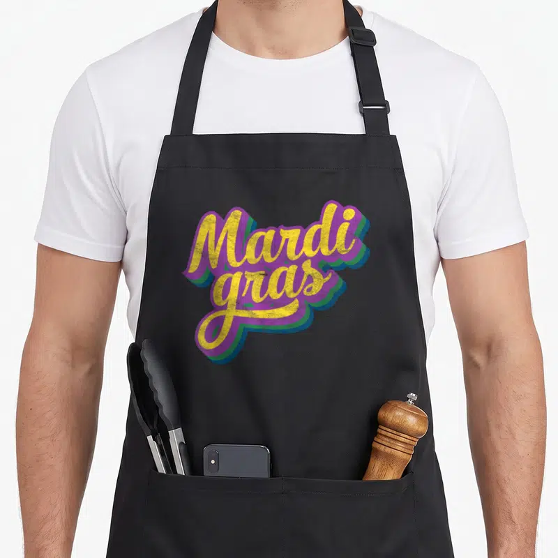 Masquerade mardi gras aprons - Yellow script text Mardi gras with purple green blue 3D shadow block — shown on a black cotton canvas apron against a white background