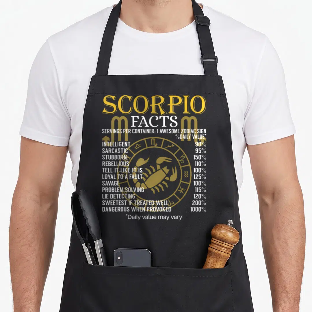 Scorpion zodiac aprons - Yellow scorpion and zodiac wheel behind white nutrition facts text listing personality traits — shown on a black cotton canvas apron against a white background
