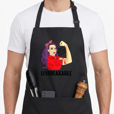 Unbreakable aneurysm awareness apron - Woman with purple hair flexing arm, red ribbon, Brain Aneurysm Warrior script — shown on a black cotton canvas apron against a white background