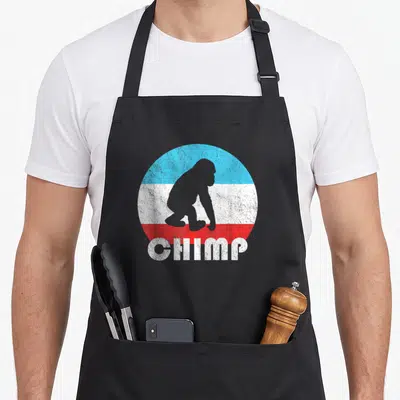 Baby chimpanzee dad apron - Grey chimp silhouette in blue white red distressed circle with CHIMP text — shown on a black cotton canvas apron against a white background
