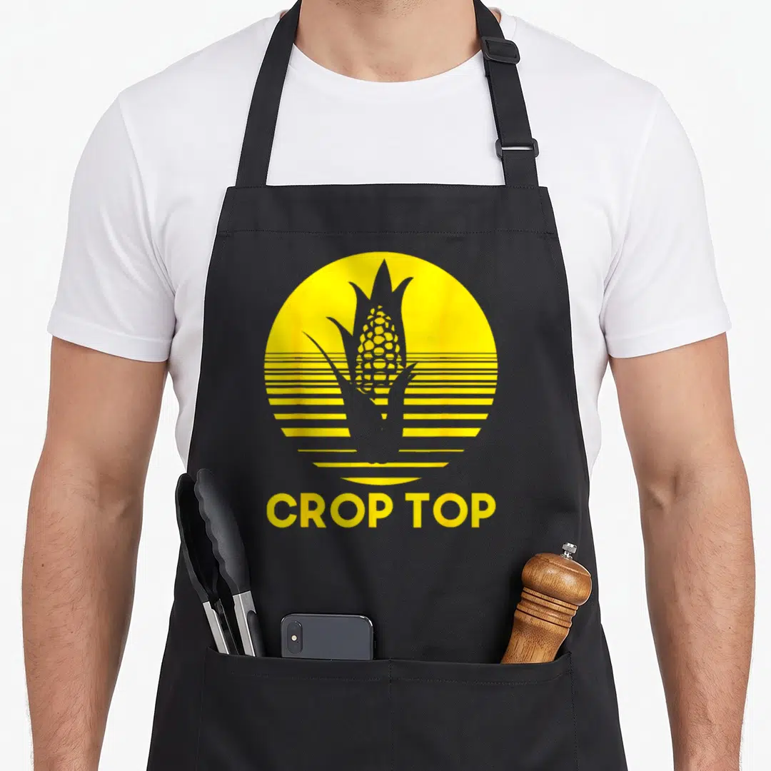 Corn farmer apron - Yellow circle with corn silhouette and CROP TOP text below — shown on a black cotton canvas apron against a white background