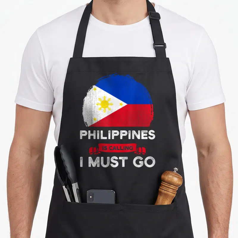 Calling pride apron - Distressed Philippine flag circle above PHILIPPINES IS CALLING I MUST GO text on red ribbon — shown on a black cotton canvas apron against a white background