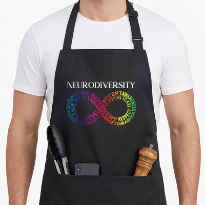 Neurodivergent rainbow apron - Infinity symbol formed by words ACCEPT, LOVE, RESPECT in rainbow colors — shown on a black cotton canvas apron against a white background
