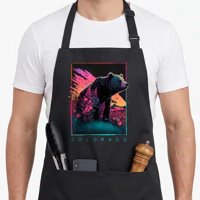 Retrowave bear apron - Profile bear with floral elements and COLORADO text in neon sunset colors — shown on a black cotton canvas apron against a white background