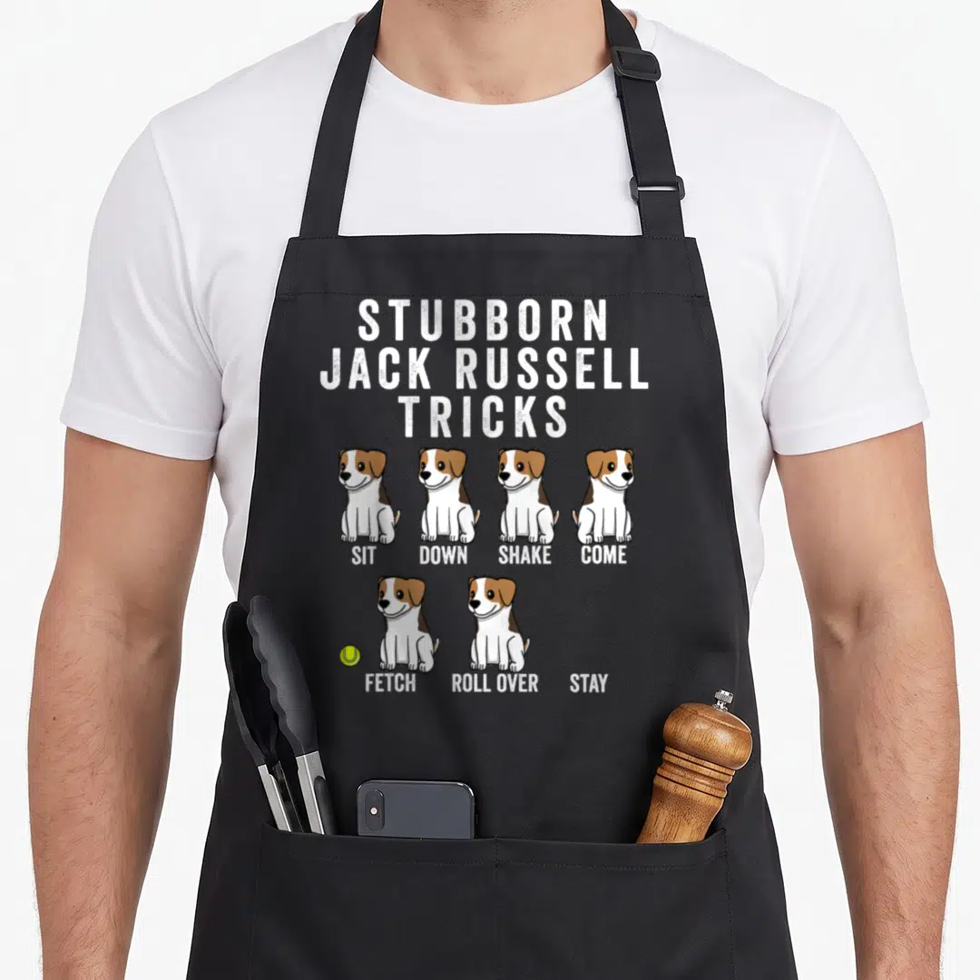 Jack dog apron - Six cartoon white and brown dogs with commands Sit Down Shake Come Fetch Roll Over Stay and a tennis — shown on a black cotton canvas apron against a white background