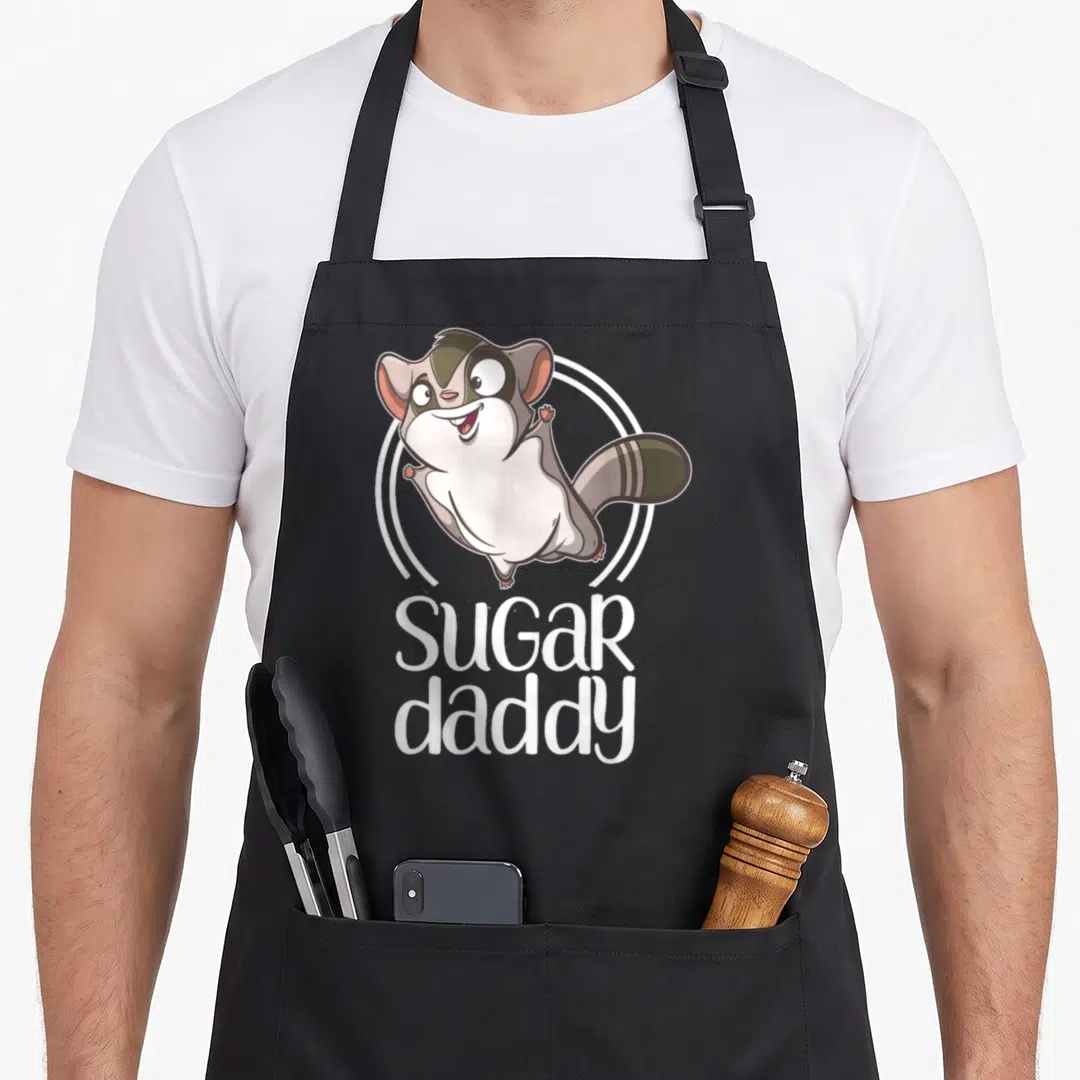 Sugar glider daddy apron - Cartoon sugar glider in white circle with SUGAR daddy text below — shown on a black cotton canvas apron against a white background