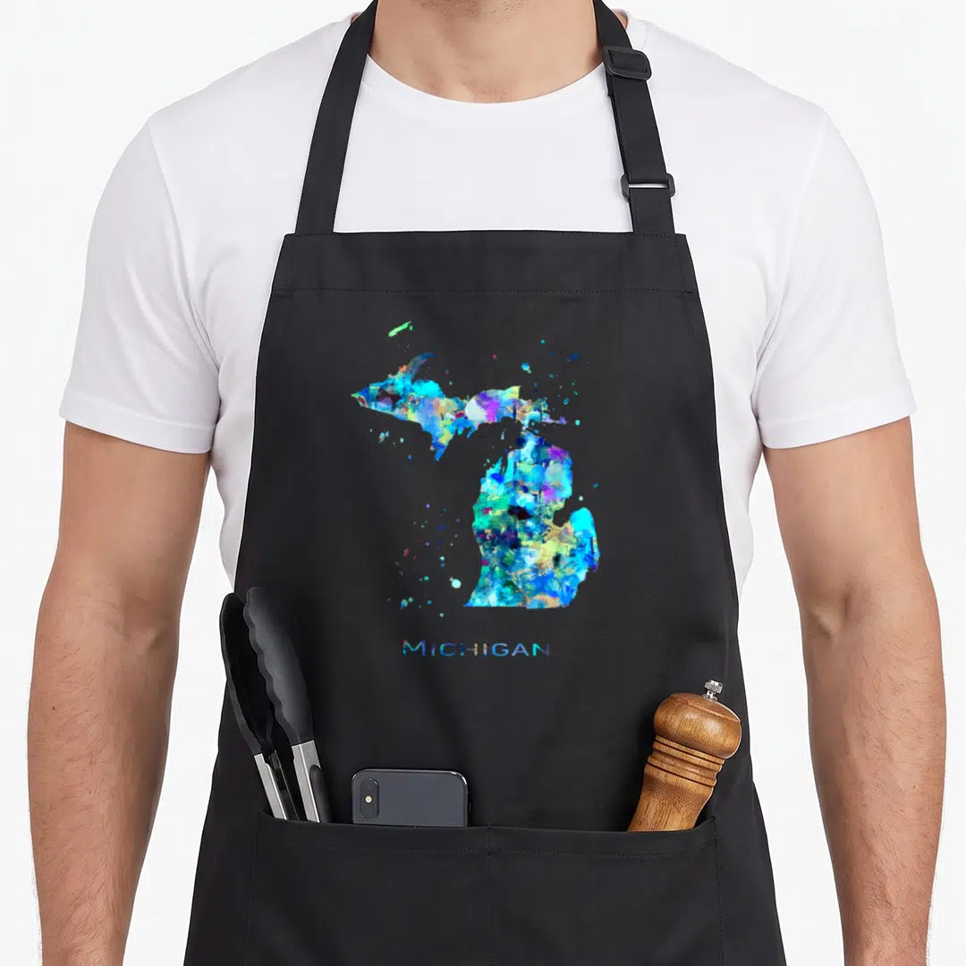 Michigan travel girl apron - Watercolor map of Michigan state in blue, cyan, yellow, purple, and green splashes — shown on a black cotton canvas apron against a white background