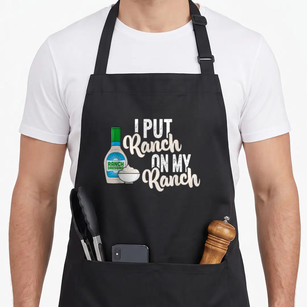 Vintage ranch dressing apron - Cartoon ranch bottle and bowl next to stacked text I Put Ranch On My Ranch in white — shown on a black cotton canvas apron against a white background