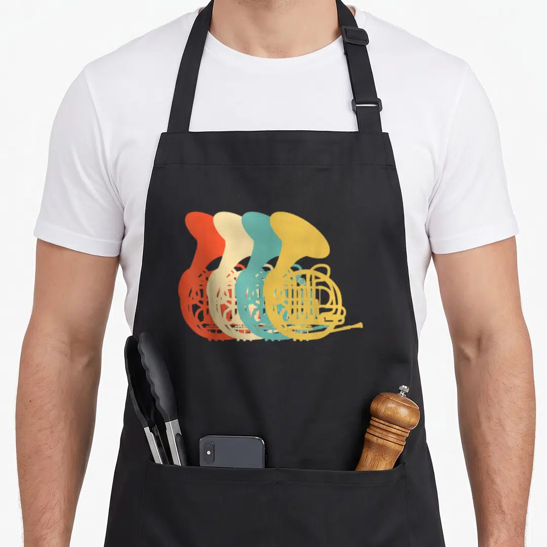 Band french apron - Four overlapping French horn silhouettes in orange, beige, teal, and yellow arranged diagonally — shown on a black cotton canvas apron against a white background