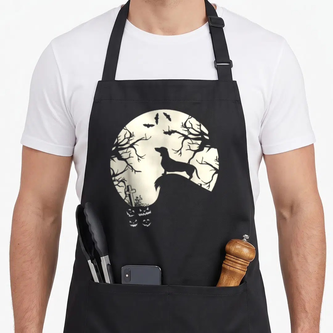 Pumpkin cheap halloween aprons - Grey dachshund silhouette on moon with graveyard cross and white jack-o-lanterns below — shown on a black cotton canvas apron against a white background
