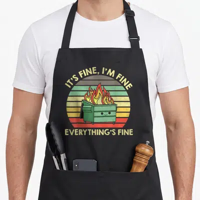 Dumpster its fine apron - Green dumpster on fire with retro sun and sarcastic text IT'S FINE I'M FINE EVERYTHING'S FINE — shown on a black cotton canvas apron against a white background
