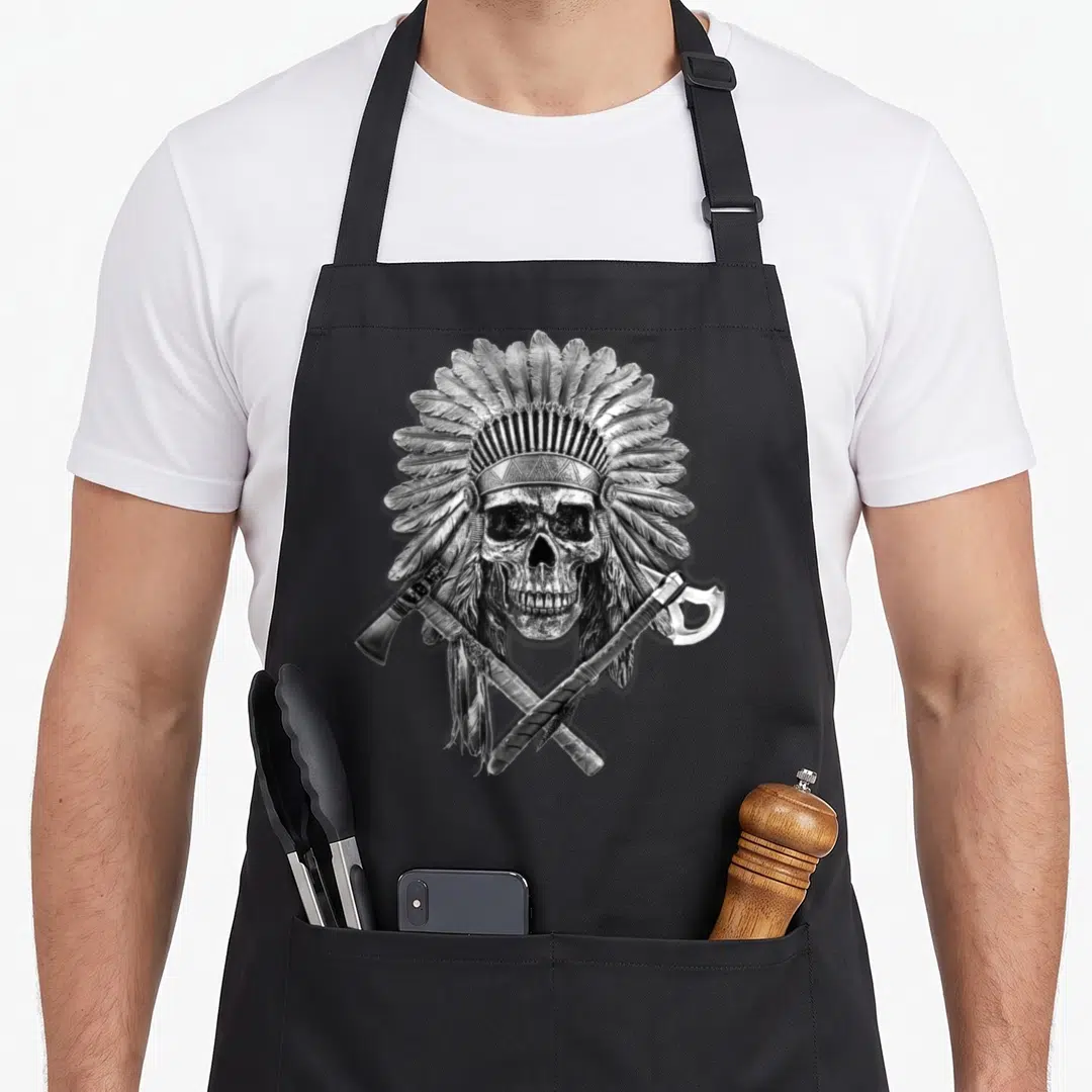 Pipe native american apron - Realistic skull with feathered headdress and two crossed tomahawks in silver grey and black — shown on a black cotton canvas apron against a white background