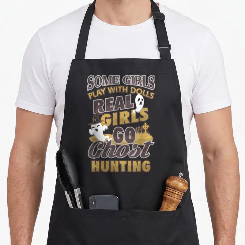 Paranormal hunter apron - Stacked brown and gold text with two white ghosts and a witch hat over a graveyard — shown on a black cotton canvas apron against a white background