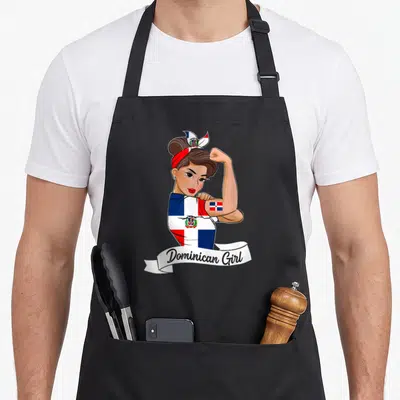 Dominicana pride apron - Cartoon woman in flag shirt flexing arm with Dominican Girl text on white ribbon — shown on a black cotton canvas apron against a white background
