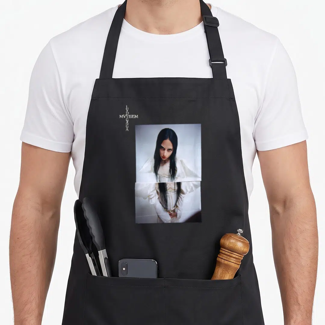 Mayhem novelty apron - Vertical LVD MVYHEM GAGA text beside a photo of a woman in a white dress — shown on a black cotton canvas apron against a white background