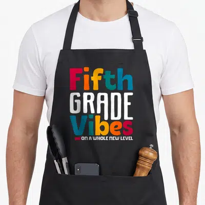 Grade day fifth apron - Stacked colorful text reading Fifth GRADE Vibes ON A WHOLE NEW LEVEL in red orange yellow green — shown on a black cotton canvas apron against a white background