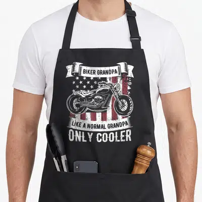 Rider biker apron - Distressed motorcycle over red white flag with Biker Grandpa Like Normal Only Cooler text ribbons — shown on a black cotton canvas apron against a white background