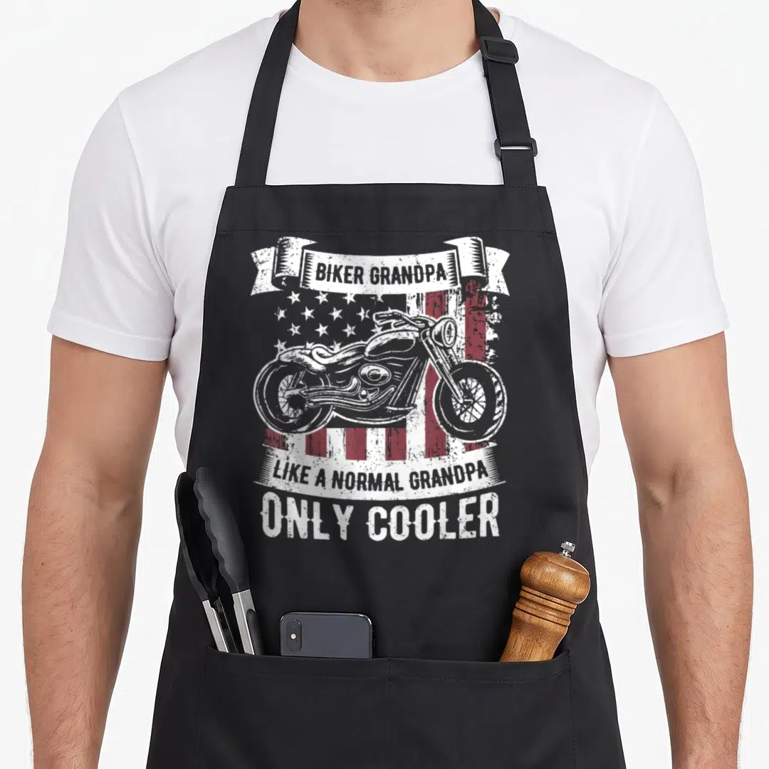 Rider biker apron - Distressed motorcycle over red white flag with Biker Grandpa Like Normal Only Cooler text ribbons — shown on a black cotton canvas apron against a white background